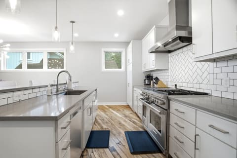 Modern kitchen with white cabinetry, quartz countertops, stainless steel appliances, and herringbone tile backsplash.