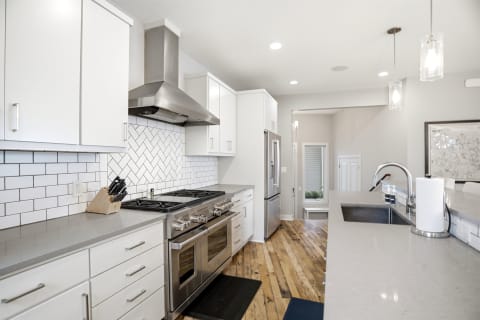 A contemporary kitchen with white cabinets, a herringbone tile backsplash, and stainless steel appliances.
