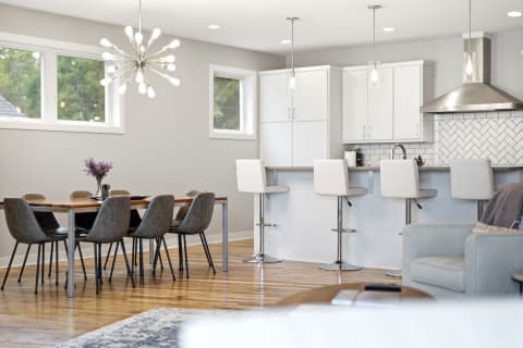 Modern open-concept kitchen and dining area with white cabinetry, sleek dining table, and stylish lighting fixtures.