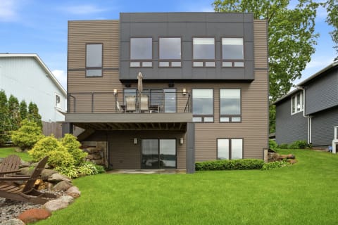 Three-story vacation rental featuring a balcony and well-manicured lawn.
