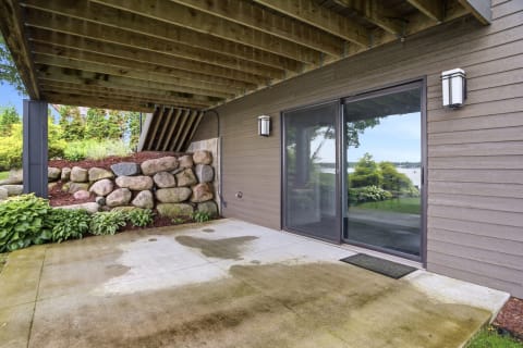 Ground-floor patio entrance featuring a stone wall, concrete surface, and lush landscaping with lake views.
