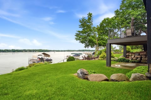 A picturesque lakefront scene with a covered dock, green lawn, and tranquil waters under a blue sky.