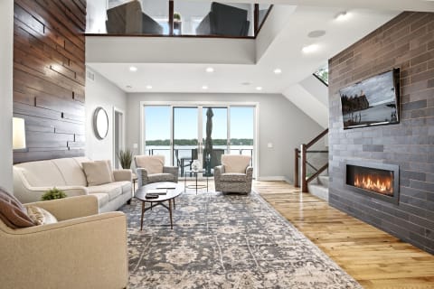 Bright living room with a sofa, armchairs, coffee table, fireplace, and lake view through glass doors.