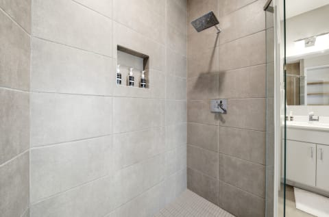 A modern shower with neutral tiles, a rainfall shower head, and a built-in niche for toiletries.