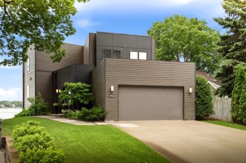 Modern architectural home with wood siding surrounded by lush greenery and mature trees.