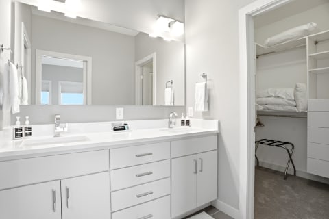 Modern bathroom featuring dual sinks, white cabinetry, and a connected walk-in closet.