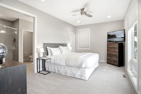 A serene bedroom with a plush bed, ceiling fan, flat-screen TV, and ensuite bathroom.