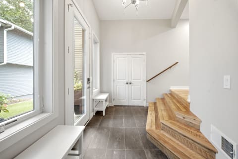 Bright entryway featuring a wooden staircase, white walls, and large windows allowing natural light.