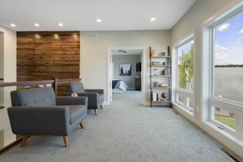 Stylish living area with gray chairs, wooden decor, and windows overlooking a lake.