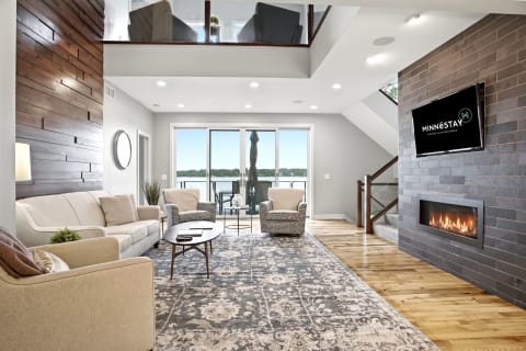 A modern living room with a fireplace, plush sofa, and lake views from glass doors.
