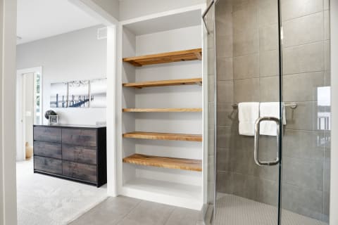 Modern bathroom with spacious glass shower, wooden shelves, and a calming color palette.