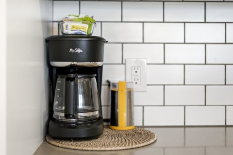 A black Mr. Coffee maker with a glass carafe and sweetener packets on a kitchen countertop.