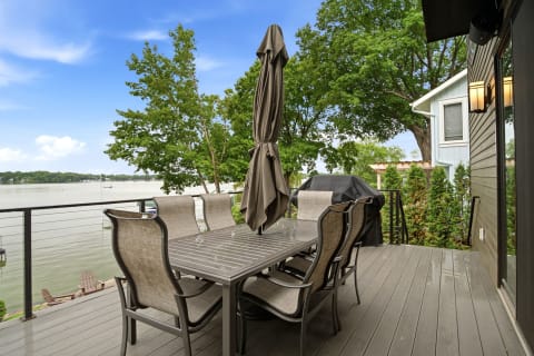 Outdoor deck with dining table, grill, and lake views surrounded by greenery.