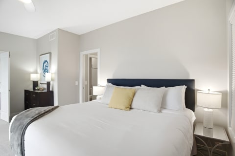 A serene bedroom with a king-sized bed, soft white linens, and modern decor including lamps and artwork.
