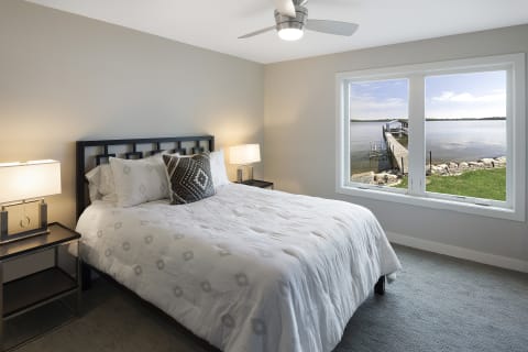 Cozy bedroom with a view of a wooden dock by the water.