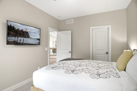 A serene bedroom featuring a plush bed with floral bedding, a mounted television, and a doorway leading to a bathroom.