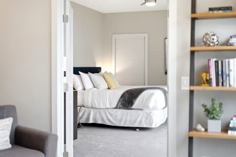 A serene bedroom featuring a cozy bed with white linens and soft gray throw, brightened by natural light.