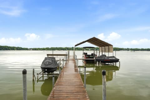 Wooden dock leading to a covered boat slip on a peaceful lake with jet skis.