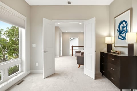 A spacious and serene room with open double doors, plush carpeting, and modern decor.