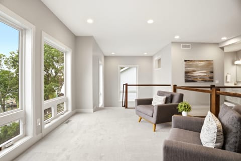 An inviting upstairs lounge with gray seating, large windows, and decorative artwork that offers treetop views.