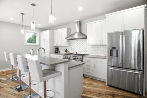 Modern kitchen with white cabinets, stainless steel appliances, and a central island under pendant lighting.