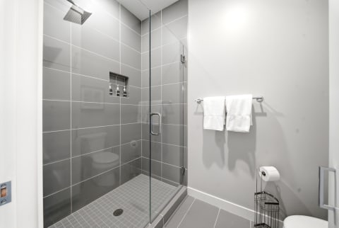 A modern, spacious walk-in shower with gray tile walls and a rainfall showerhead, featuring neatly hung white towels.