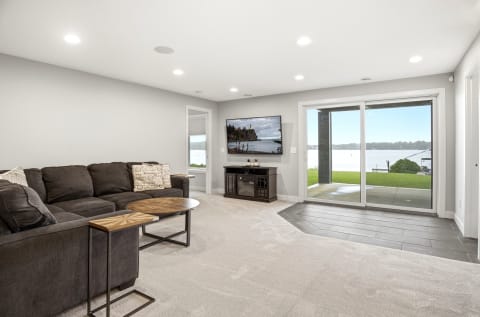 Bright living room with a dark sectional couch, a decorative side table, and a view of the water through sliding glass doors.