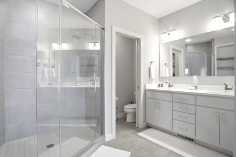 A modern bathroom featuring a walk-in shower, dual vanity sinks, and sleek grey tiles with bright lighting.