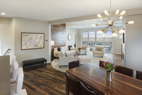 Modern living space featuring a white sectional couch, wooden dining table, and scenic view of water through sliding glass doors.