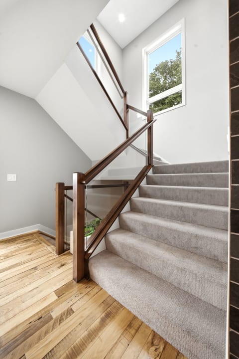 A modern staircase with carpeted steps and a wood and glass railing bathed in natural light.