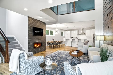Open-concept living area featuring a grey-tiled fireplace, modern furniture, and a bright kitchen.