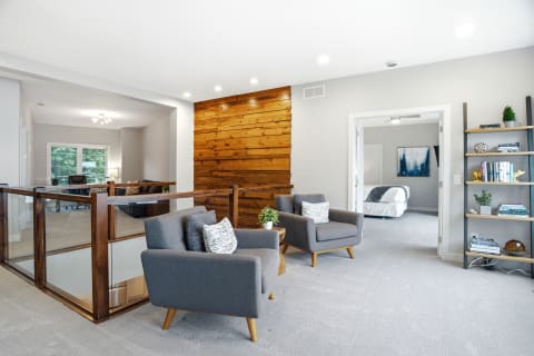 Bright upper-level lounge with mid-century chairs and wooden accent wall, overlooking a cozy bedroom area.