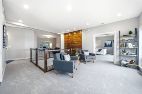 A spacious upstairs area with modern chairs, wood paneling, and a view into a cozy room.