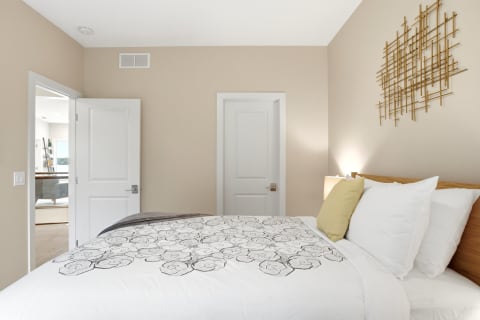A cozy bedroom with beige walls, a bed adorned with white linens and floral designs, and stylish gold wall art.
