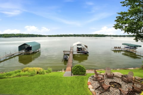 Lakeside view featuring docks, boats, and a fire pit area surrounded by grass.