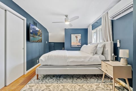 Modern bedroom featuring a double bed, nightstand with lamp, and flat-screen TV on deep blue walls.