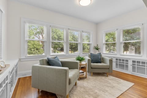 A cozy seating area with green armchairs, a small plant, and natural light from large windows.