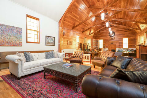 A spacious living room featuring a white Chesterfield sofa, dark leather couch, a decorative coffee table, and vibrant artwork on the walls.