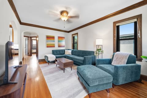 A stylish living room featuring teal furniture and wooden accents, illuminated by natural light.