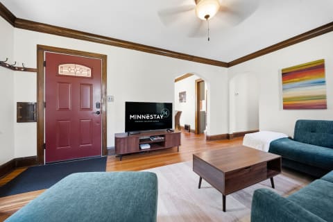 A spacious living room with a red front door, teal sofas, a wooden coffee table, and an abstract painting on the wall, enhancing the inviting ambiance.