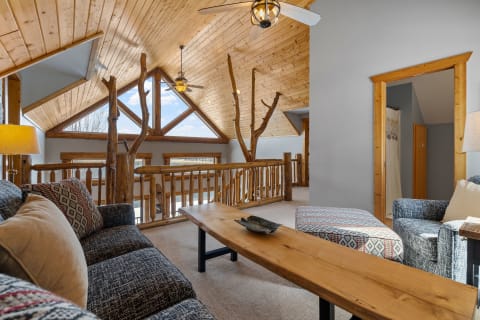 A cozy loft with a wooden ceiling, large windows, and comfortable seating.
