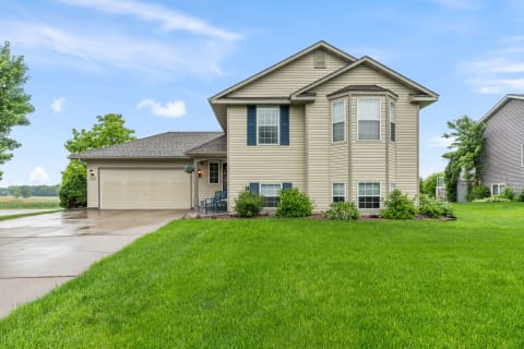 Two-story beige house with dark blue shutters and vibrant green lawn.
