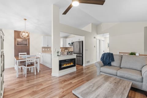 A cozy modern living room with a dining area and kitchen, highlighted by a gray sofa and an electric fireplace.