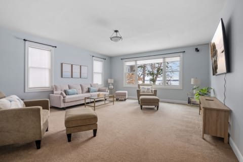 A spacious living room featuring a beige sectional sofa, accent chair, and large windows with blue walls.