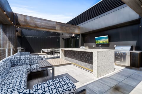 Stylish outdoor kitchen with granite bar seating, BBQ grill, and cozy lounge area on a rooftop.