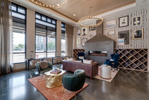 An elegant lounge with plush seating, a modern fireplace, and a striking chandelier, illuminated by natural light from large windows.
