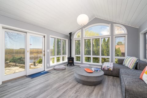 A bright sunroom with large windows, a sectional sofa, and a concrete coffee table.