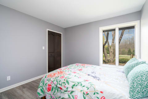Cozy bedroom featuring floral patterned duvet and a large window overlooking greenery.