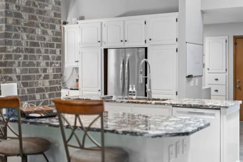 Modern kitchen with granite island, white cabinets, and stainless steel appliances.