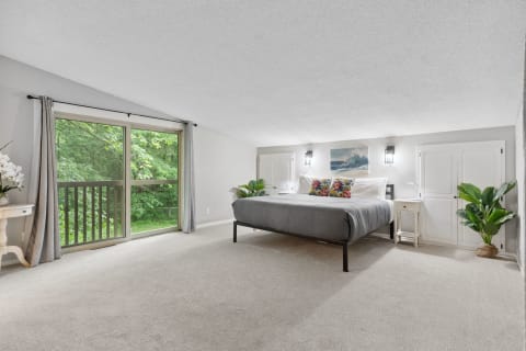 Modern bedroom with a gray bed and a view of green foliage outside.
